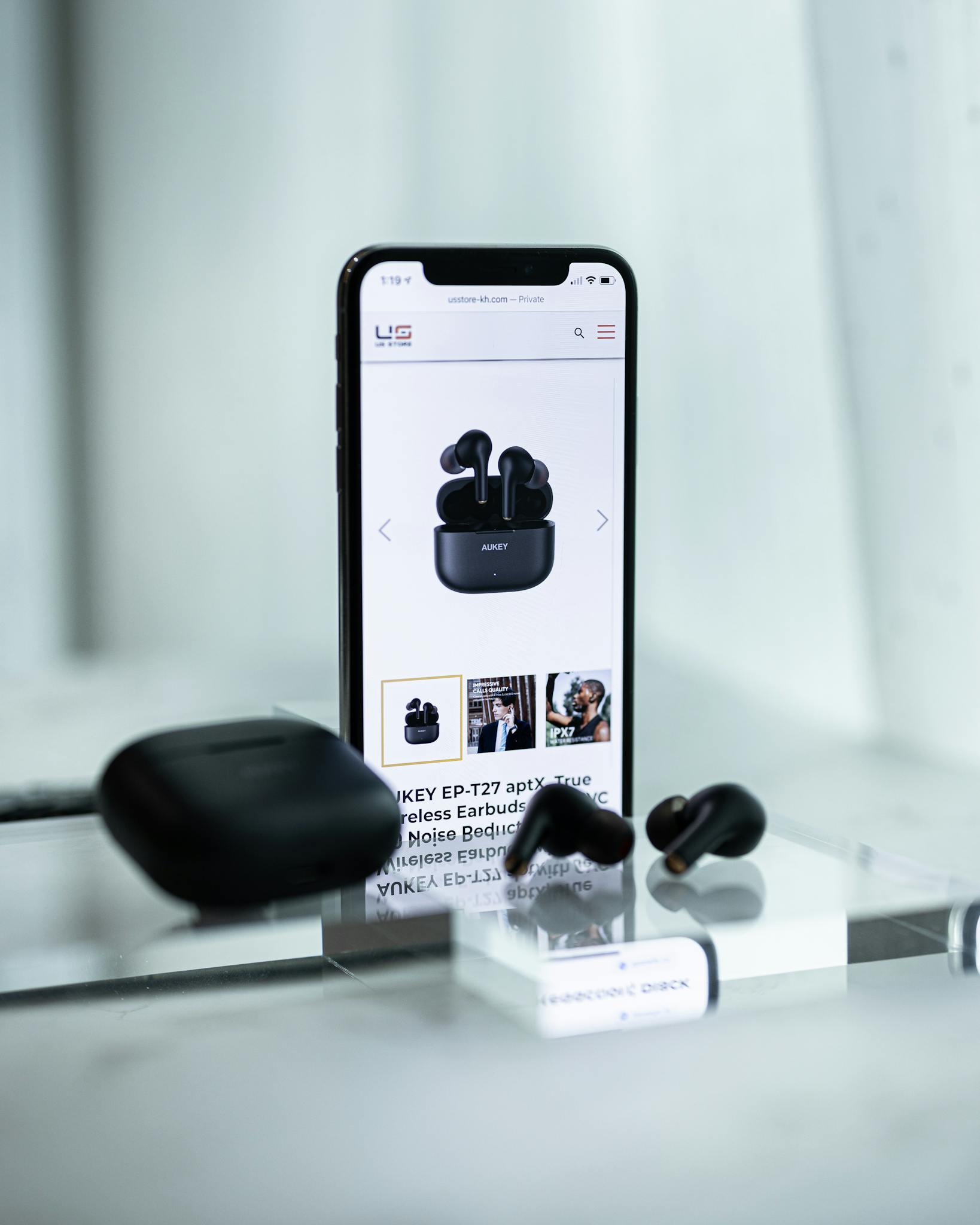 Close-up of a smartphone displaying wireless earbuds details, surrounded by sleek earbuds and a case.